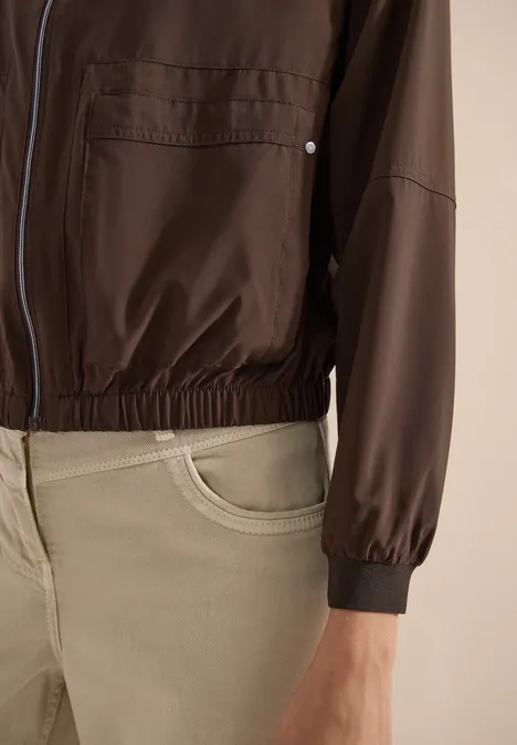 Blouson in Unifarbe mit Zipper brown cacao Nahaufnahme einer Person in brauner Jacke mit Reißverschluss und beiger Hose.