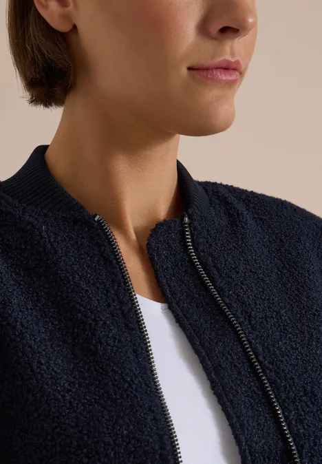 Nahaufnahme einer Person in weißem Shirt und dunkelblauer, strukturierter Jacke mit Reißverschluss.