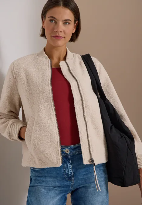 Vrouw in beige jas, rood topje, jeans en zwarte tas.