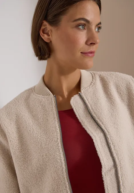 Een vrouw in een beige teddyfleecejas en rood topje kijkt opzij.