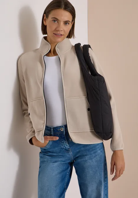 Fleecejacke mit Zipper und Stehkragen powder beige Frau in beiger Jacke, weißem T-Shirt und blauen Jeans mit schwarzer Umhängetasche.