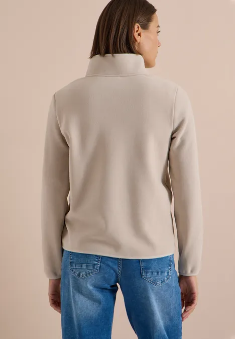 Fleecejacke mit Zipper und Stehkragen powder beige Eine Frau steht mit dem Rücken zur Kamera und trägt einen hellbeigen Fleecetop mit Stehkragen und blauen Jeans.
