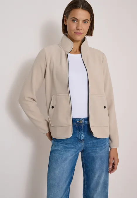 Fleecejacke mit Zipper und Stehkragen powder beige Frau trägt beige Jacke, weißes Shirt und blaue Jeans vor hellem Hintergrund.