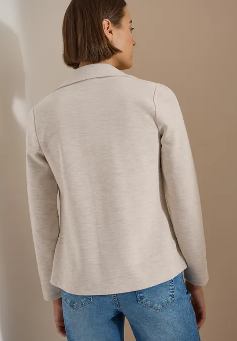 Vrouw gezien van achteren met beige blazer en spijkerbroek voor een neutrale achtergrond.