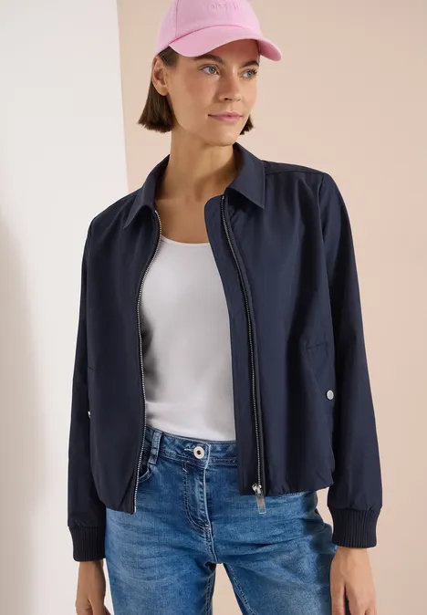 Blouson mit Hemdblusenkragen urban dark blue Eine Frau in Jeans, weißem Top, navyblauer Bomberjacke und rosa Cap, Gesicht verschwommen