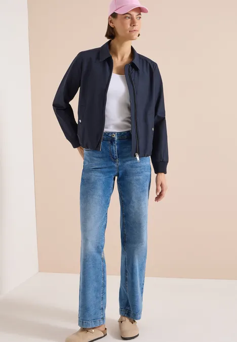 Blouson mit Hemdblusenkragen urban dark blue Frau in dunkelblauer Jacke, weißem T-Shirt und blauen Jeans vor hellem Hintergrund.