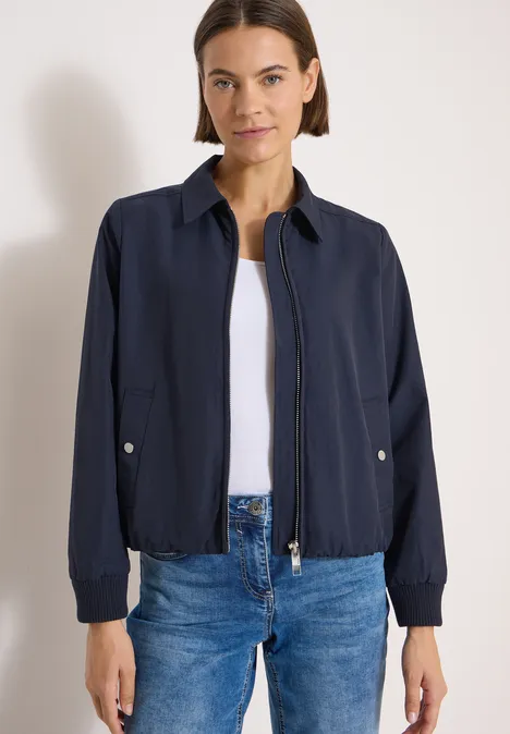 Blouson mit Hemdblusenkragen urban dark blue Frau trägt dunkelblaue Jacke über weißem Shirt und Jeans vor hellem Hintergrund.