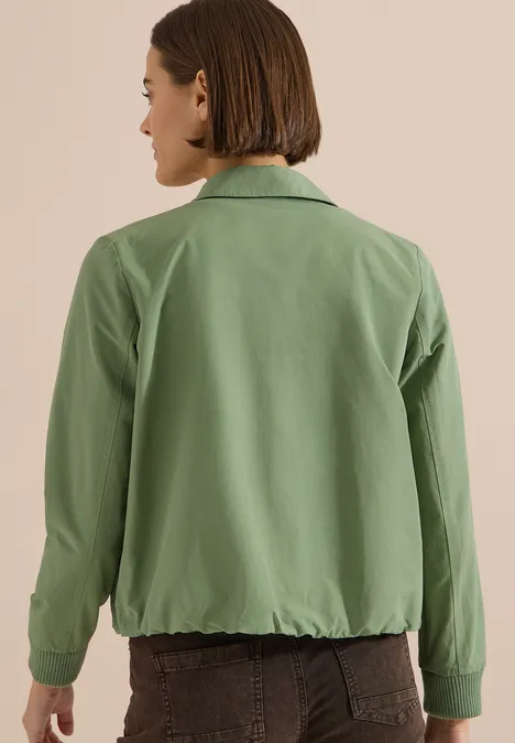 Persoon met kort haar draagt een groen jack en een bruine broek, achteraanzicht.