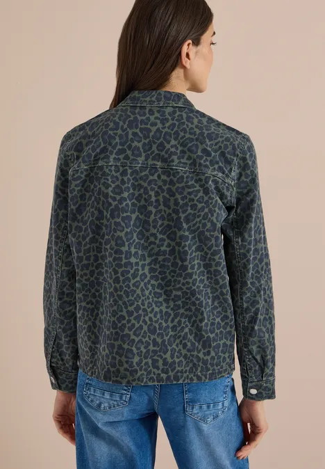Frau von hinten in blau-grün gemusterter Jeansjacke vor beigem Hintergrund.