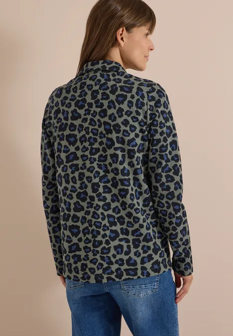 Rugaanzicht van een vrouw in een blauwgroene luipaardprint blazer en spijkerbroek.