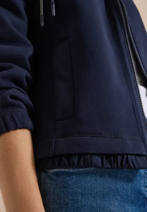 Nahaufnahme einer Person in dunkelblauer Jacke und blauer Jeans.