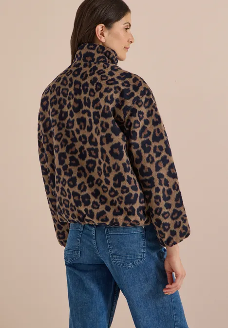 Frau trägt Rückansicht einer braun-schwarzen Leoparden-Fleecejacke und blauen Jeans.