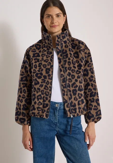 Frau trägt eine kurze, leopardgemusterte Jacke mit Reißverschluss und weiten Ärmeln, kombiniert mit blauen Jeans.