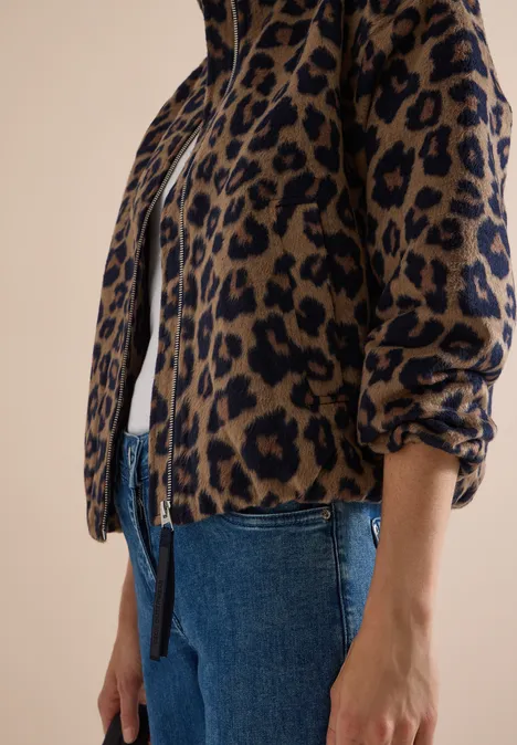 Teilansicht einer Person in blauer Jeans und leopardgemusterter Jacke mit Reißverschluss.