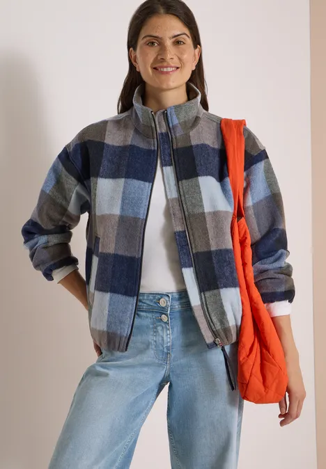 Frau in karierter blau-grauer Jacke, weißem Shirt, hellen Jeans und roter Tasche über der Schulter