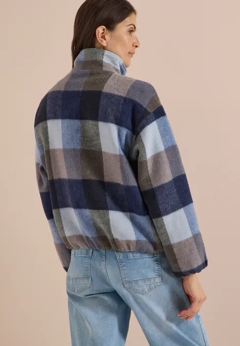 Ein Mann von hinten in kariertem Fleecejacke mit Stehkragen und elastischem Bund, dazu Jeans.
