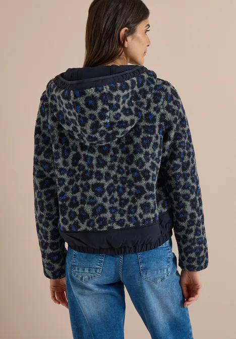 Eine Frau von hinten in blauer Leo-Jacquard-Jacke mit Kapuze und Jeans.