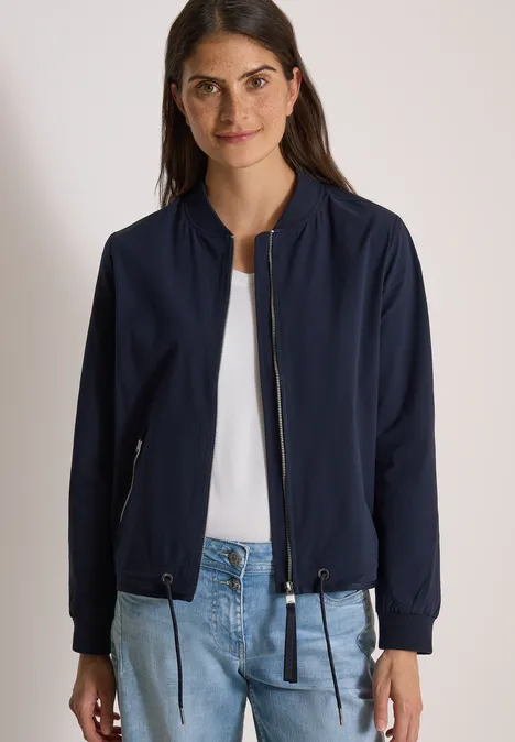 Frau trägt marineblaue Bomberjacke, weißes Shirt und blaue Jeans.