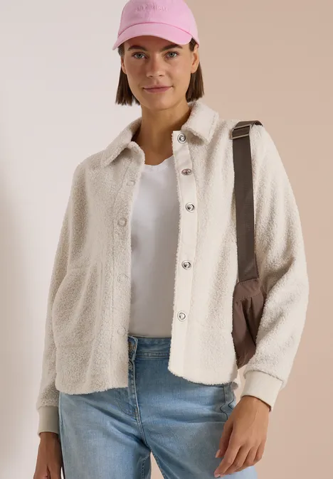 Teddy-Overshirt mit Knopfleiste teddy vanilla white Frau mit rosa Cap, weißem T-Shirt, cremefarbener Hemdjacke, blauen Jeans und Umhängetasche.