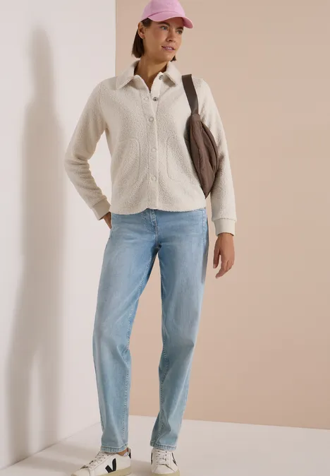 Teddy-Overshirt mit Knopfleiste teddy vanilla white Frau in beige Fleecejacke, hellblauen Jeans, rosa Cap und Schultertasche vor neutralem Hintergrund.