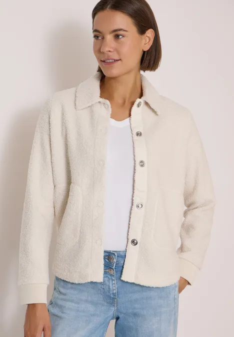 Teddy-Overshirt mit Knopfleiste teddy vanilla white Frau trägt eine cremefarbene Teddy-Jacke über weißem Top und Jeans vor neutralem Hintergrund.