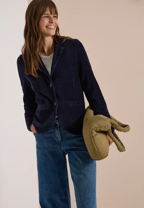 Jerseycord Blazer in Unifarbe urban dark blue Frau trägt dunkelblauen Blazer, Jeans und hält eine grüne Mütze mit Abklapp-Ohren.