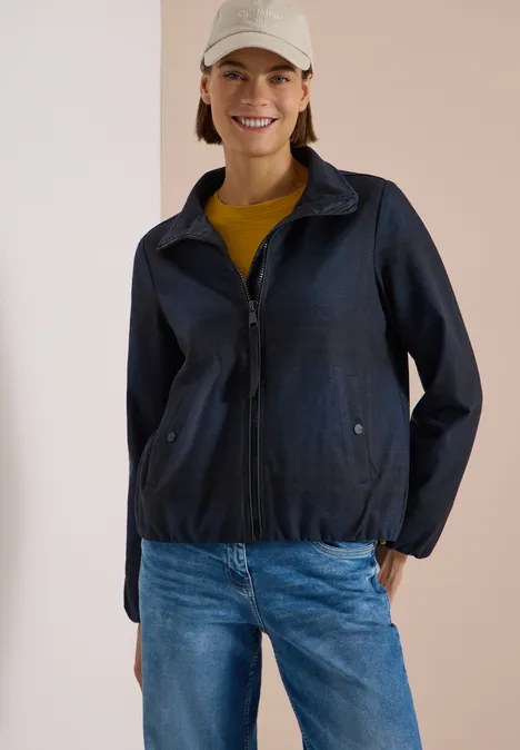 Karierte Jacke in Wolloptik mit Stehkragen urban dark blue melange Frau in dunkelblauer Jacke, Jeans und Basecap vor hellem Hintergrund, lächelnd und entspannt.
