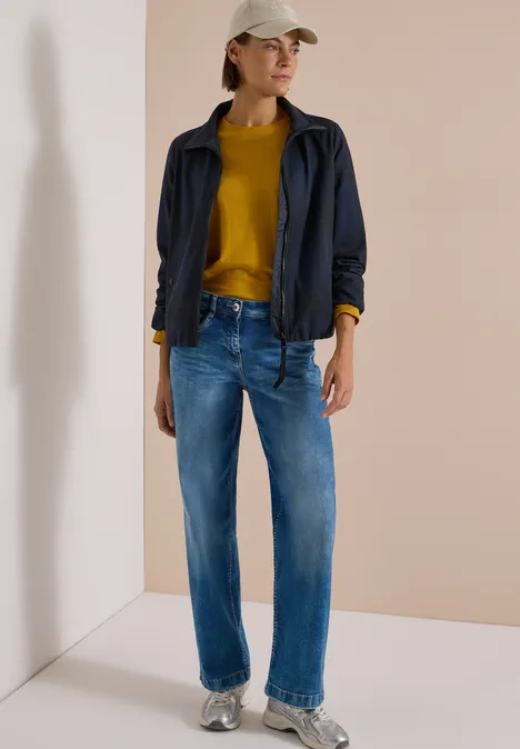 Karierte Jacke in Wolloptik mit Stehkragen urban dark blue melange Frau trägt blaue Jeans, senfgelber Pullover, dunkelblaue Jacke und beige Mütze vor hellem Hintergrund.
