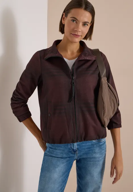 Karierte Jacke in Wolloptik mit Stehkragen red wine melange Frau in legerer Jacke, Jeans und Schultertasche lehnt entspannt an einer weißen Wand.