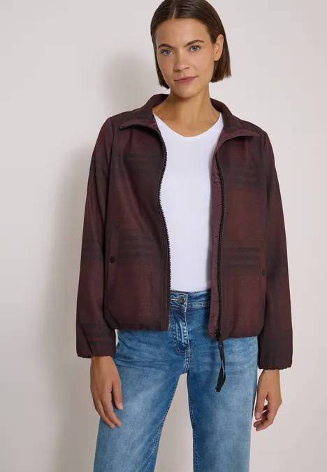 Karierte Jacke in Wolloptik mit Stehkragen red wine melange Frau in kariertem, burgunderfarbenem Blouson über weißem T-Shirt und blauen Jeans, lächelnd vor hellem Hintergrund.