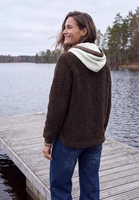 Teddy-Overshirt mit Scuba-Kapuze berry red Frau in braunem Fleece-Hoodie steht lächelnd auf einem Steg am See, umgeben von Bäumen und Wasser.