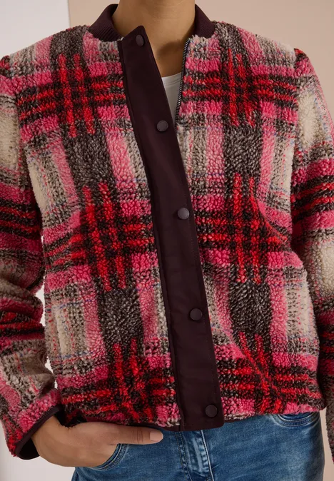 Frau trägt karierte rosa-rote Bouclé-Jacke mit lila Knopfleiste und blauen Jeans.