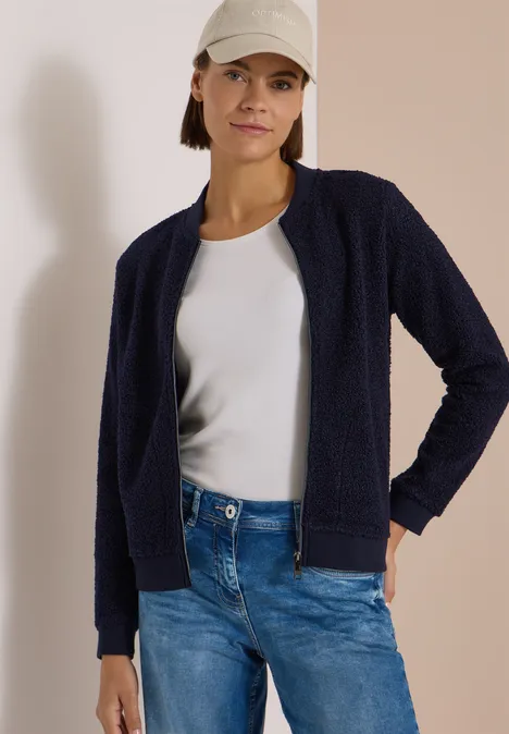 Femme en gilet bleu marine, t-shirt blanc, jean et casquette béige.