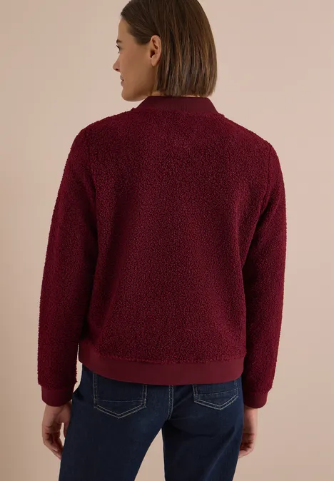 Femme vue de dos portant une veste en peluche bordeaux et un jean.