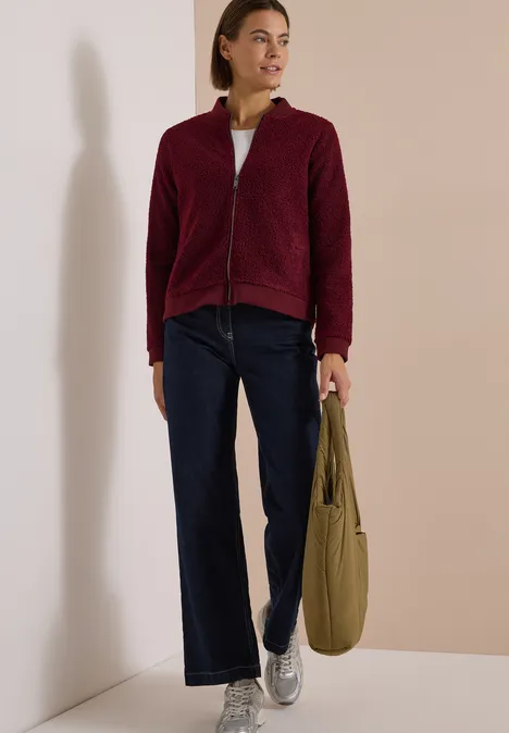 Femme en veste polaire bordeaux, jean large et baskets argentées, portant un sac kaki.