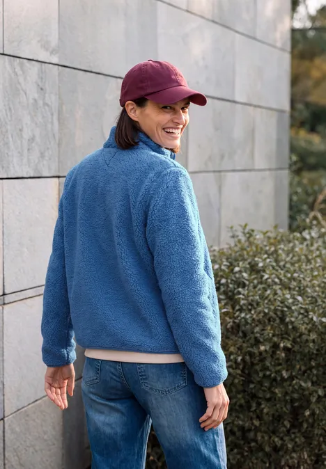 Frau in roter Kappe und blauem Fleece-Anorak dreht sich lächelnd zur Kamera im Freien.