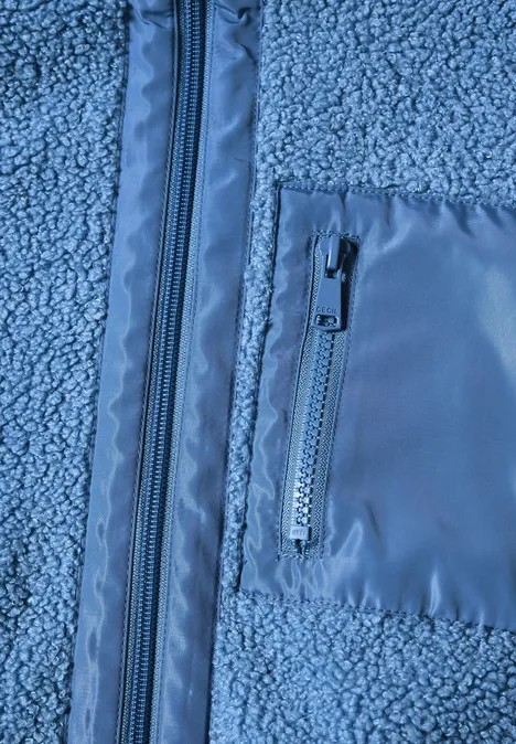 Nahaufnahme einer blauen Fleecejacke mit Hauptreißverschluss und aufgesetzter Reißverschlusstasche.