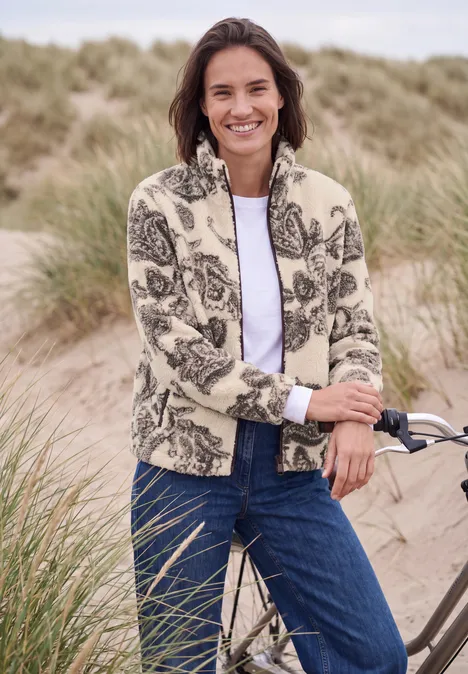 Teddyjasje met opstaande kraag en patroon teddy vanilla white Vrouw lacht in bloemenfleece en spijkerbroek naast fiets op duinenstrand.