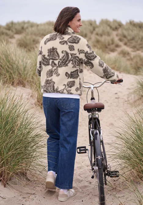 Teddyjasje met opstaande kraag en patroon teddy vanilla white Een vrouw duwt haar fiets over een duinpad omgeven door helmgras.