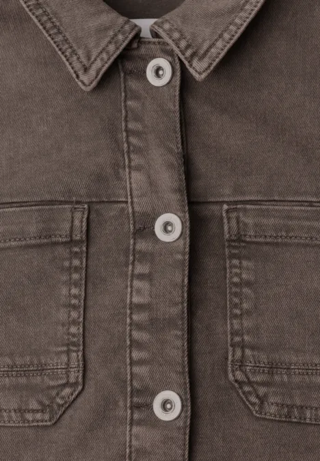 Nahaufnahme einer braunen Jeansjacke mit Kragen, Knopfleiste und zwei aufgesetzten Brusttaschen.