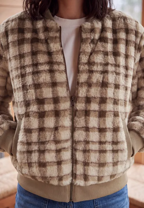 Person trägt eine beige-weiße karierte Fleece-Bomberjacke über weißem T-Shirt.