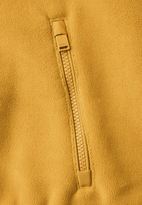 Fleecejas met capuchon en softshell-details golden honey Nahaufnahme einer senfgelben Fleecejacke mit Reißverschlusstasche.