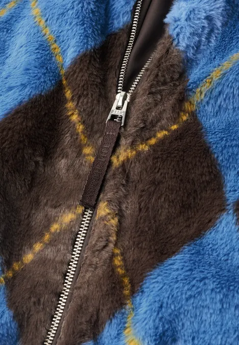 Nahaufnahme einer flauschigen Jacke mit blau-braunem Rautenmuster und Reißverschluss