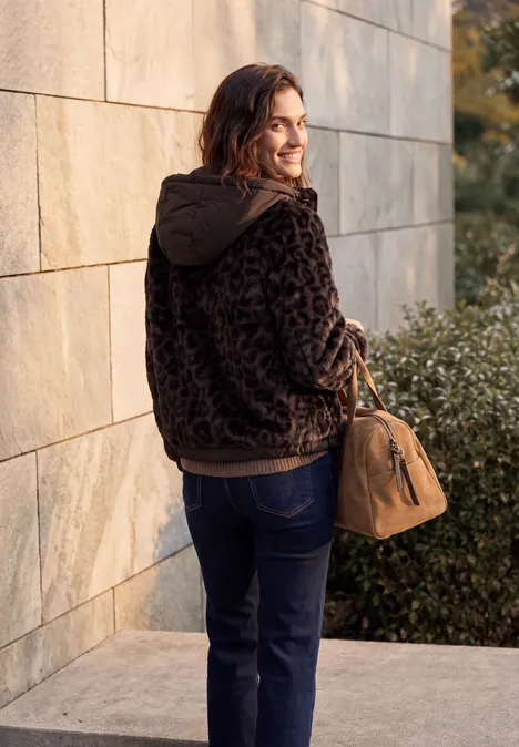 Fake Fur Jacke mit Softshell-Kapuze truffle brown Eine Frau mit brauner Tasche und dunklem, gemustertem Kapuzen-Pullover steht vor einer Hauswand und schaut zurück.
