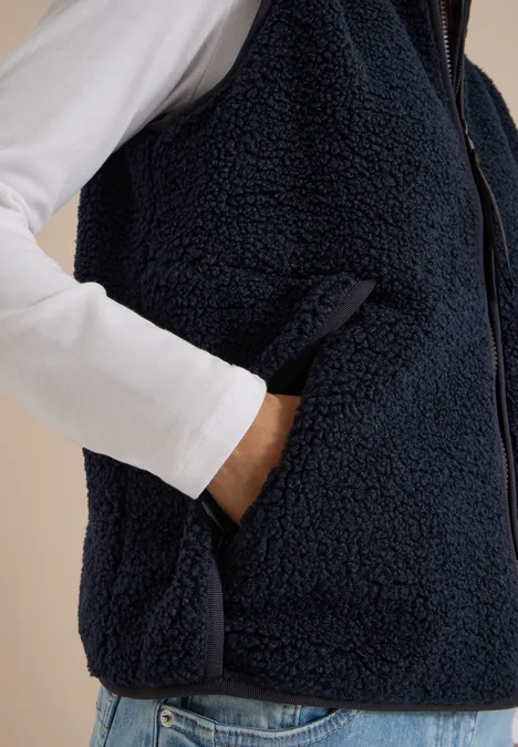 Dunkelblaue Teddy-Fleece-Weste mit Reißverschluss über weißem Langarmshirt, Hand in Tasche.