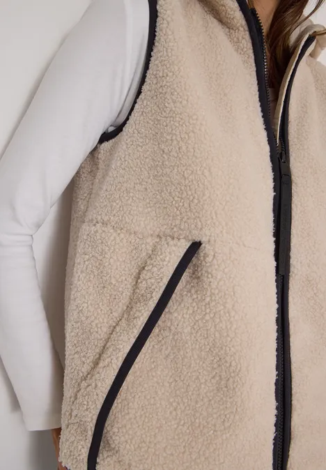 Nahaufnahme einer Person mit weißem Langarmshirt und beiger Fleece-Weste mit schwarzem Reißverschluss.