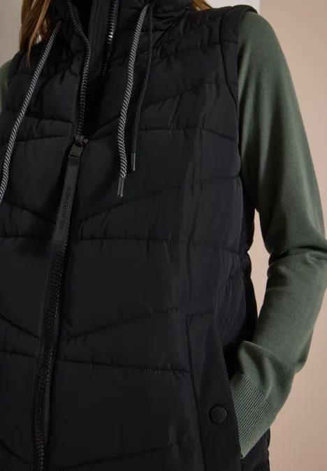 Lange Steppweste mit Stehkragen Black Schwarze gesteppte Weste mit Kapuze, darüber ein dunkelgrünes Langarmshirt.