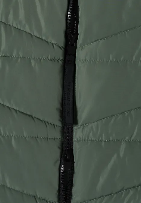 Lange Steppweste mit Stehkragen shadow khaki Grüne gesteppte Jacke mit schwarzem Reißverschluss im Close-up.
