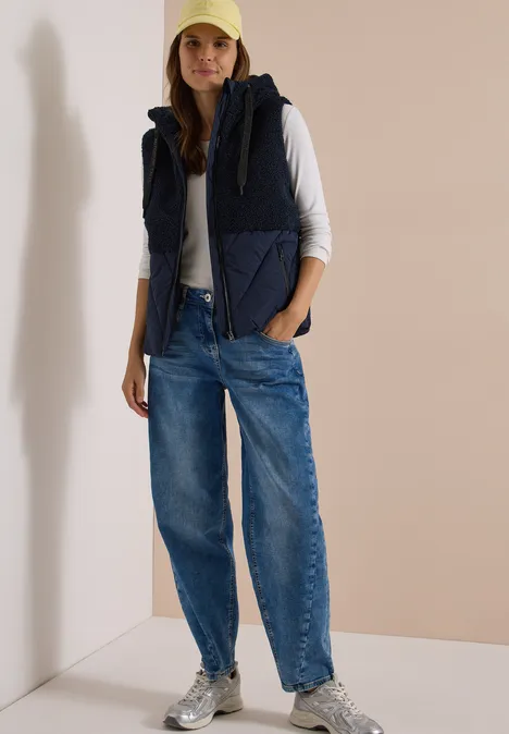 Teddy-Weste mit Steppteil und Zipper dark navy blue Frau im lässigen Outfit: Jeans, weiße Langarmshirt, wattierte Weste, Cap und Sneaker vor neutralem Hintergrund.