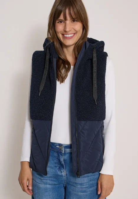 Teddy-Weste mit Steppteil und Zipper dark navy blue Eine junge Frau in weißem Shirt trägt eine marineblaue, kapuzenbesetzte Weste mit Teddy- und Steppdetails.